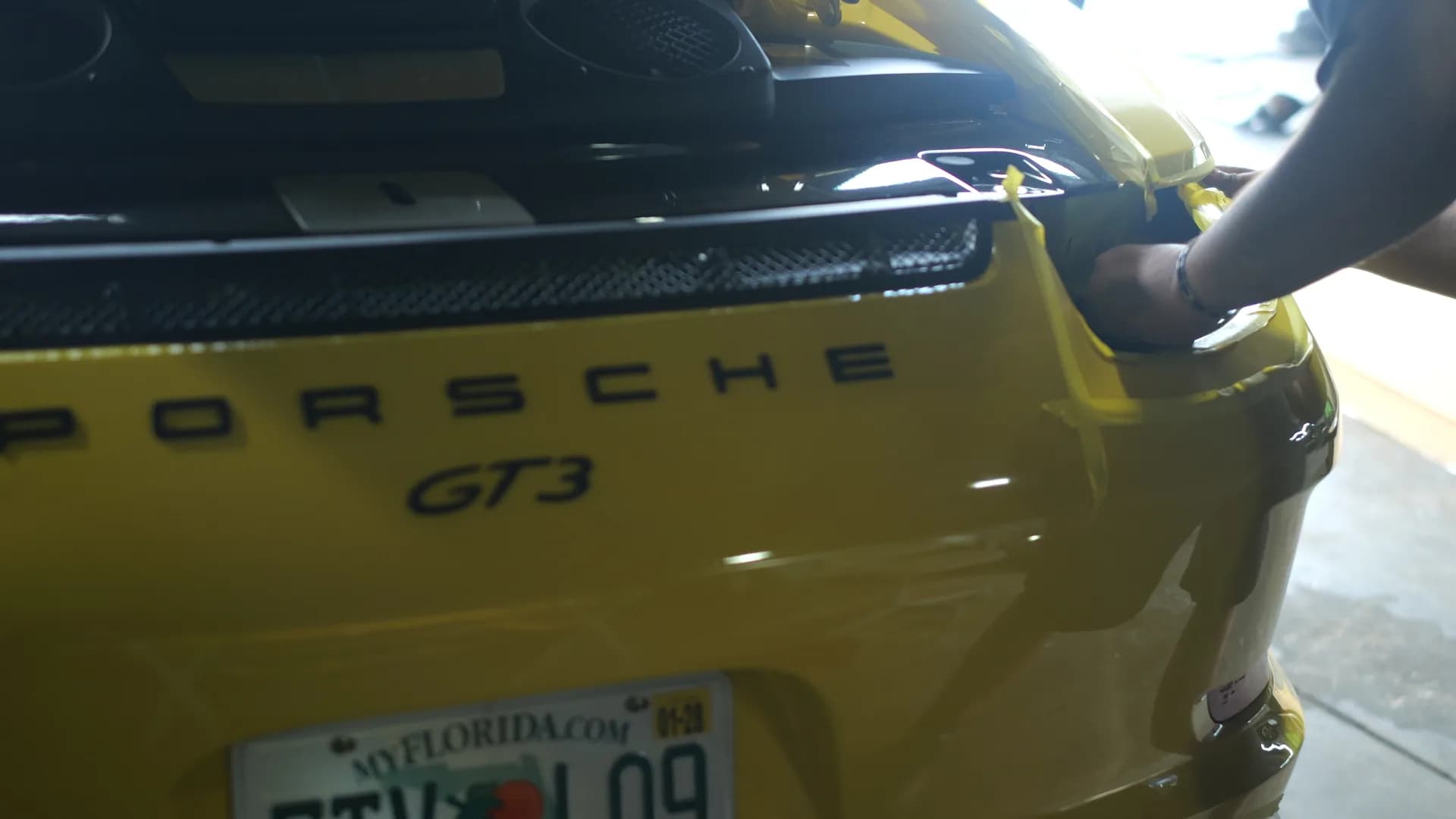 Rear deck of the yellow Porsche 911 GT3 masked with tape and a panel removed during carbon fiber fitment