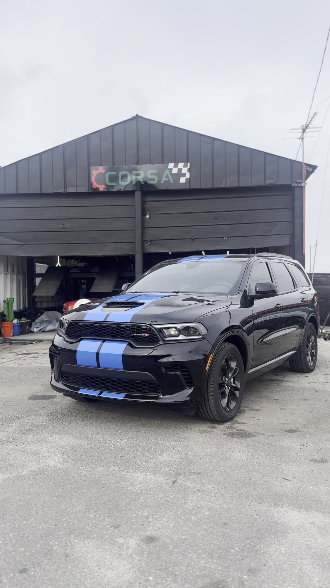 Black Dodge Durango with blue racing stripes in front of the Corsa Automotive shop in Orlando