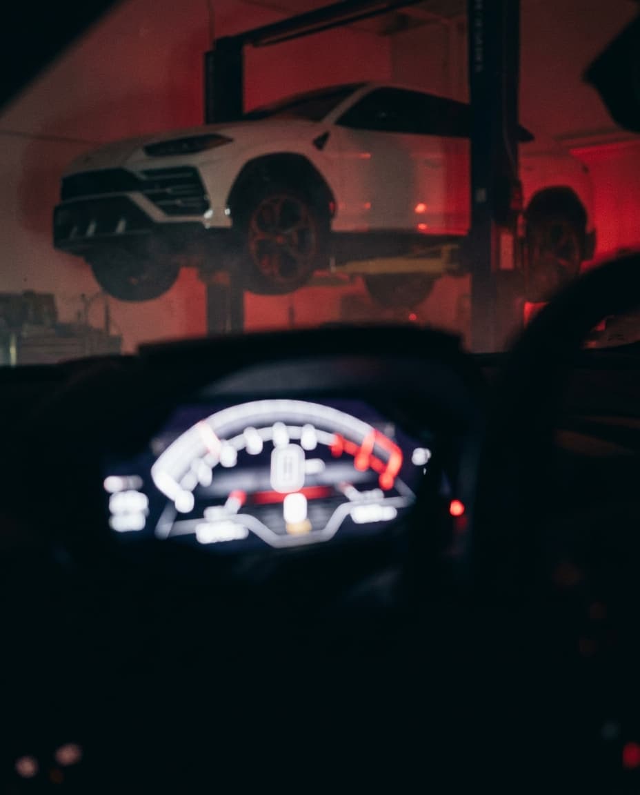 Digital instrument cluster in front of a white exotic SUV on a lift at Corsa Automotive Orlando