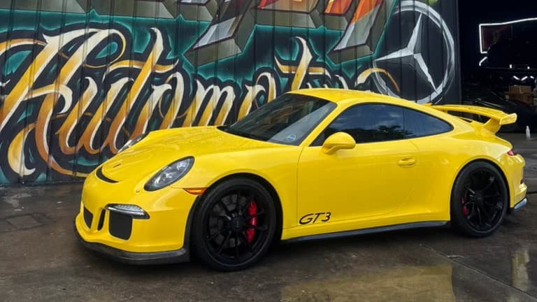 Yellow Porsche 911 GT3 parked outside Corsa Automotive in Orlando in front of the shop mural